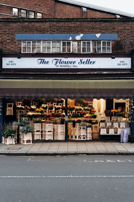 The flower shop 'The Flower Seller' of Muswell Hill features a storefront with outdoor displays of fresh flowers arranged in bouquets and potted plants. The bouquets include a variety of vibrant colou